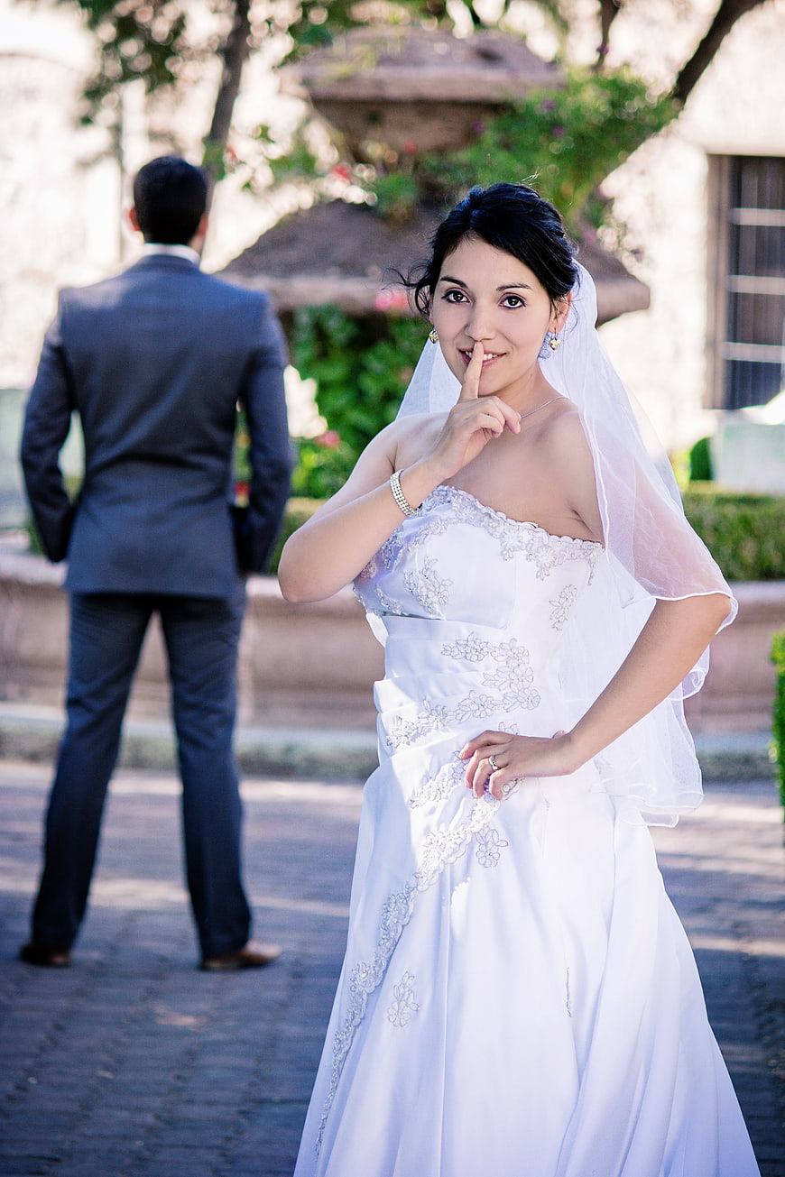 Bride Shushing Gesture with Groom in Background