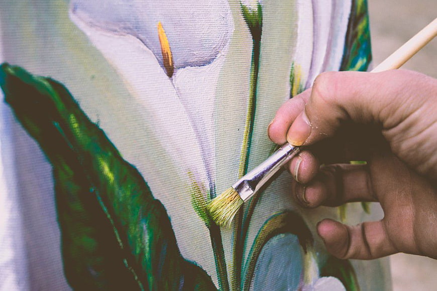 Close-up of hand painting white lily flower on canvas