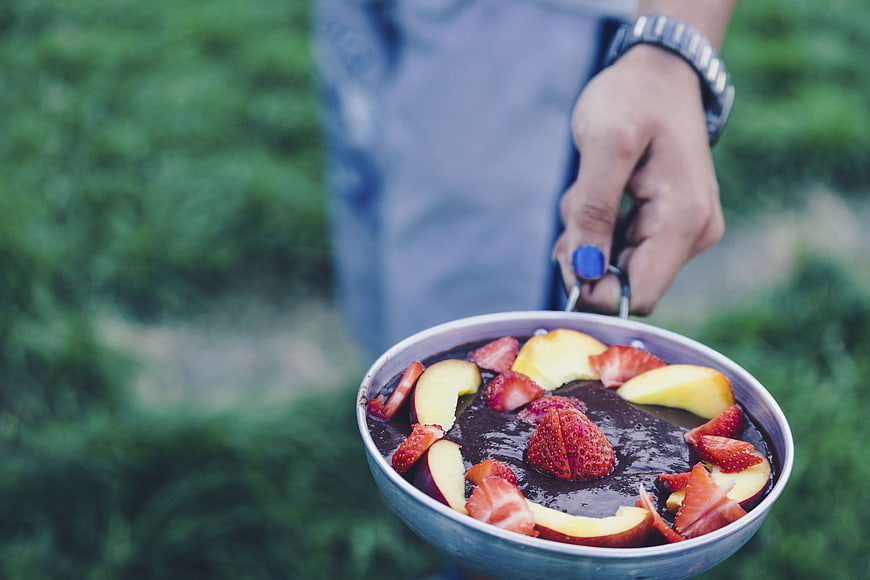 Hand holding pan of chocolate dessert with strawberries and peaches