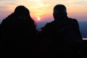 Silhouette of couple watching sunset from mountain viewpoint
