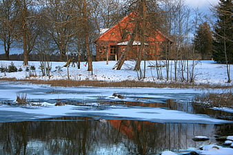 Red wooden house reflected in frozen winter river