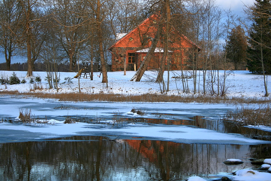 Red wooden house reflected in frozen winter river