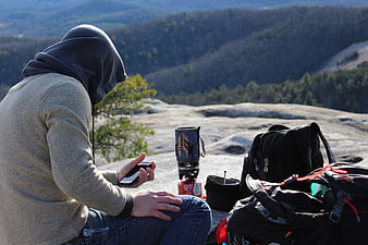 Hiker using smartphone on mountain summit with camping gear