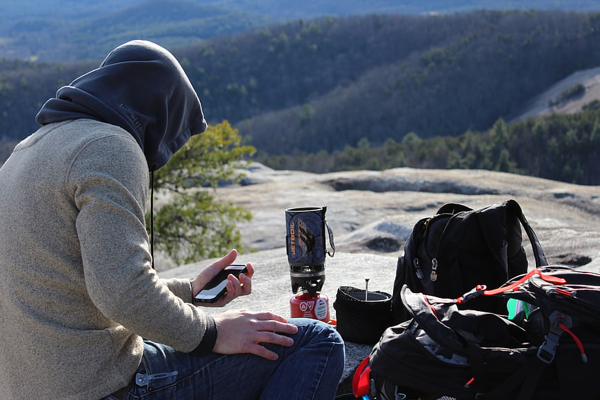 Hiker using smartphone on mountain summit with camping gear