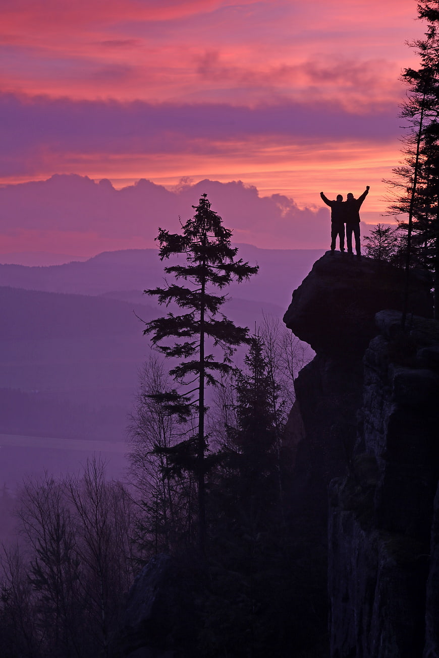Two Silhouetted Friends Celebrating on Cliff at Pink Sunrise