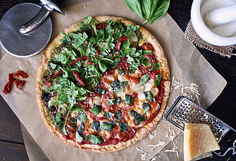 Top view of homemade pizza with pesto, tomato, and arugula