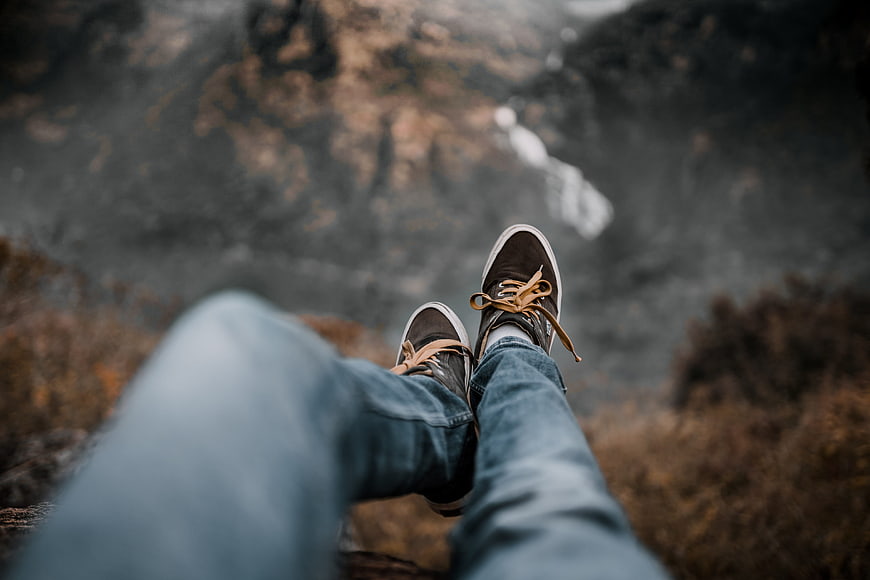 First-person view of legs dangling over a cliff edge with a waterfall in the background