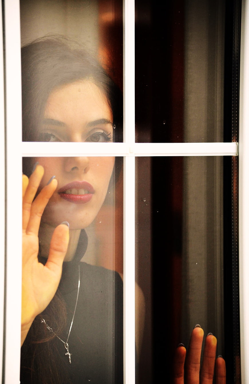 Young woman looking through window glass with hand touching pane