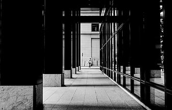 Black and white photo of a person walking through a modern architectural corridor