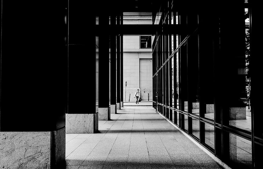Black and white photo of a person walking through a modern architectural corridor