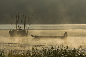 Silhouette of fisherman in boat on misty lake at sunrise