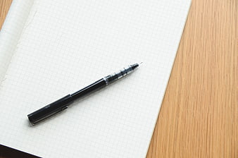 Black pen on blank graph paper notebook on wooden desk