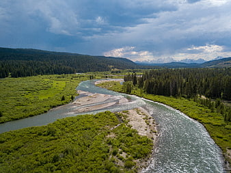 Aerial view of winding river through green valley with mountains
