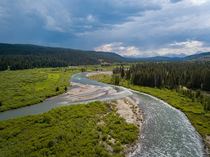 Aerial view of winding river through green valley with mountains
