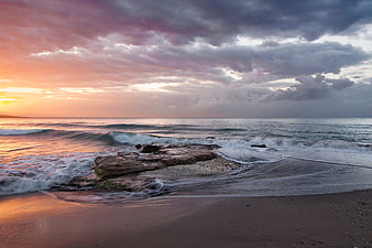 Dramatic Sunset Over Rocky Beach with Crashing Waves