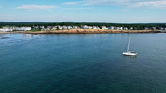 Aerial view of white sailboat on calm blue ocean near coastal town