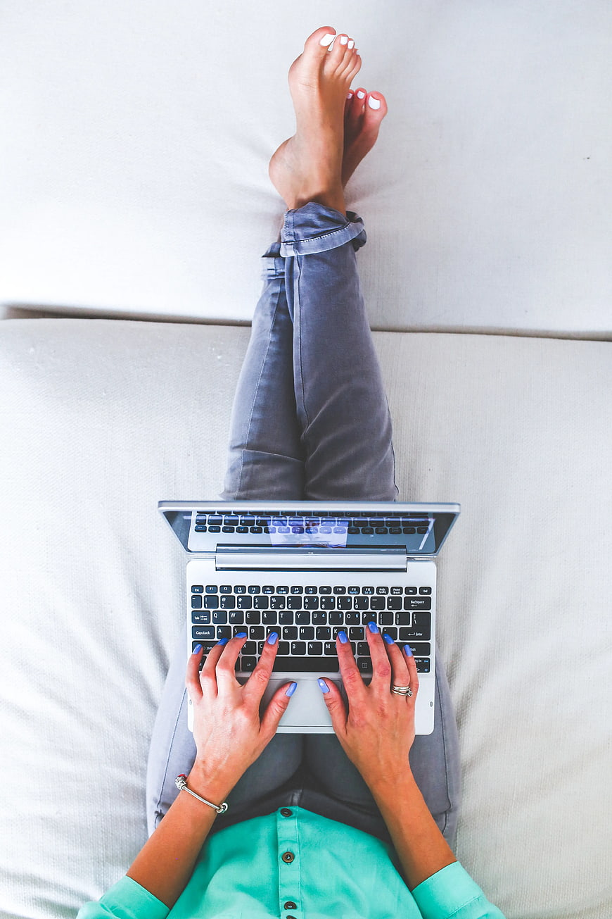 Woman typing on laptop while lying on white sofa