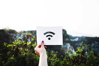 Hand holding white paper with WiFi symbol against blurred nature background