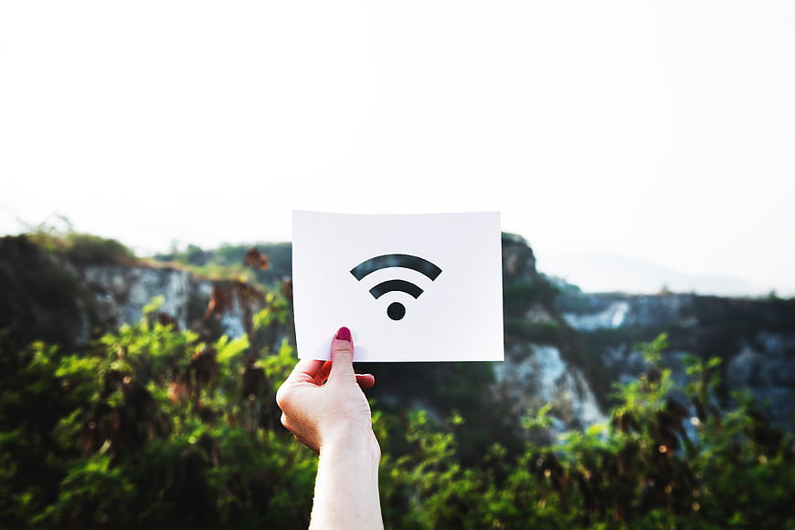 Hand holding white paper with WiFi symbol against blurred nature background