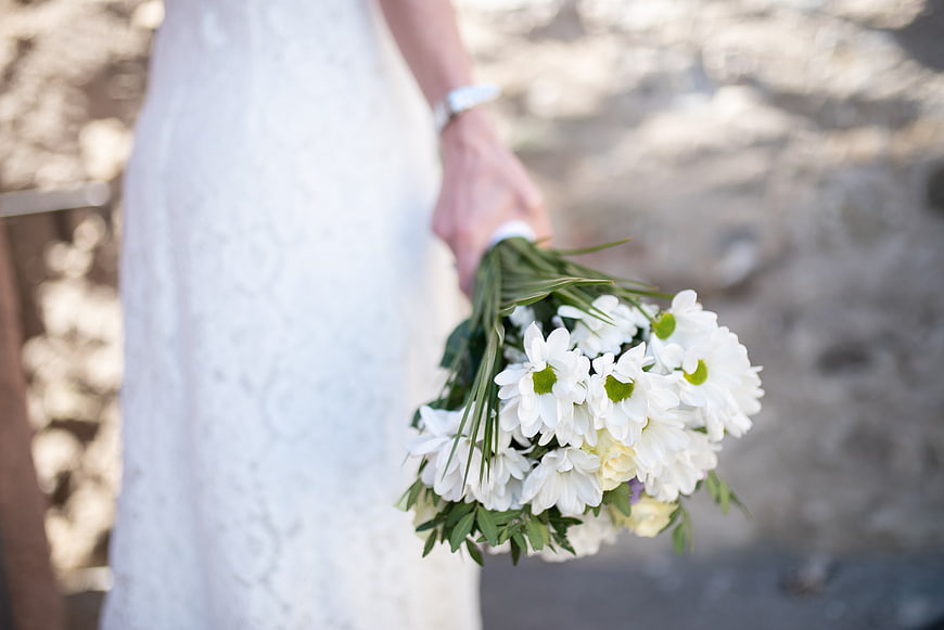 Bride holding white daisy bouquet in wedding dress