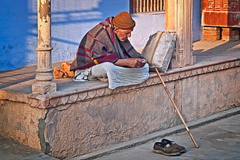 Elderly Indian man resting on stone steps with walking stick