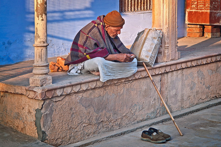 Elderly Indian man resting on stone steps with walking stick