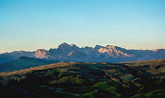 Sunlit Dolomites Mountain Range Over Rolling Green Hills