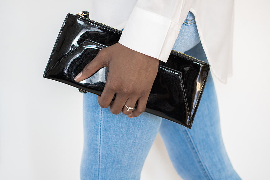 Woman holding black patent leather clutch purse