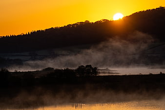 Misty Sunrise Over Silhouetted Hills and Lake