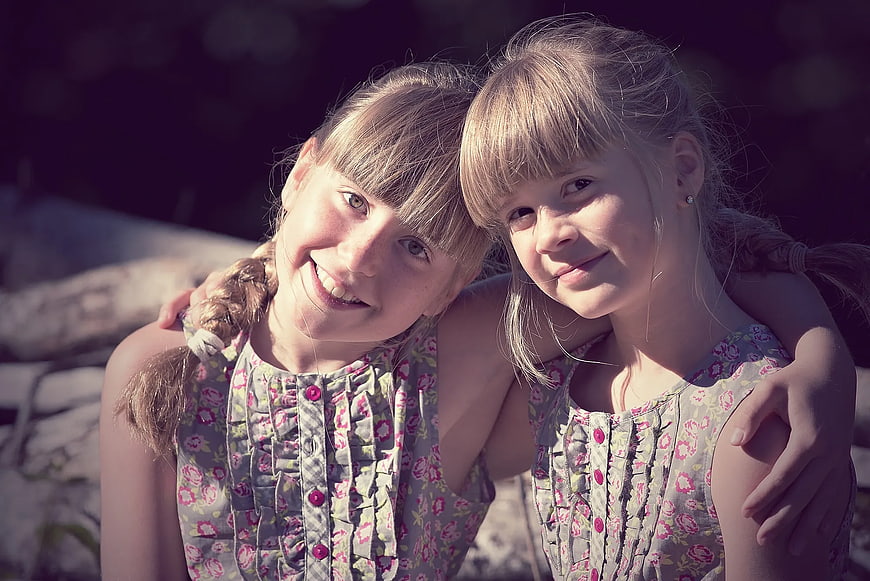 Two smiling young girls in matching floral dresses outdoors