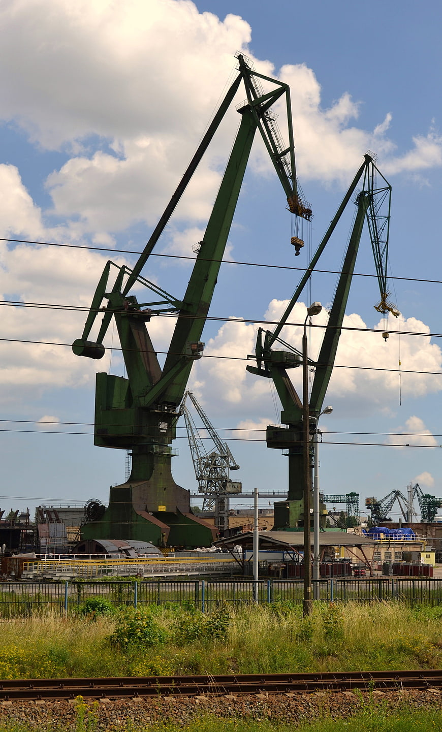 Green industrial cranes at shipyard with railway tracks