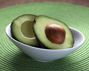 Fresh Halved Avocado in White Bowl on Green Placemat