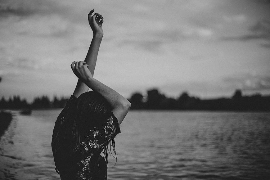 Woman with arms raised by the water in black and white