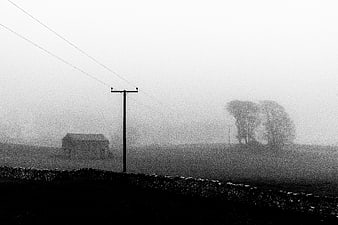Foggy rural landscape with stone wall and barn in black and white