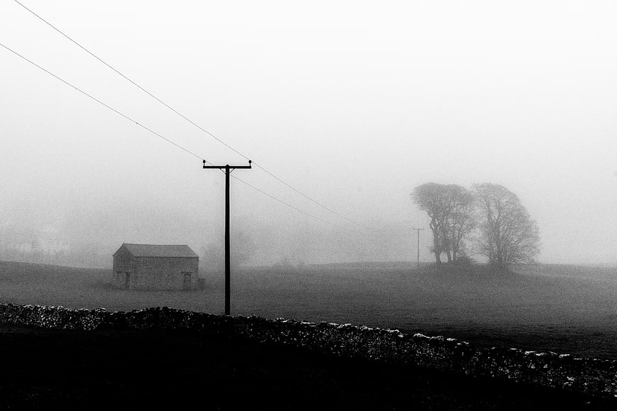 Foggy rural landscape with stone wall and barn in black and white