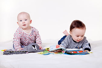 Two cute babies playing with colorful cloth books on white background