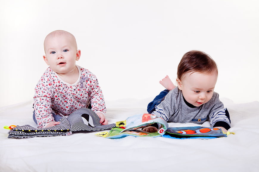 Two cute babies playing with colorful cloth books on white background