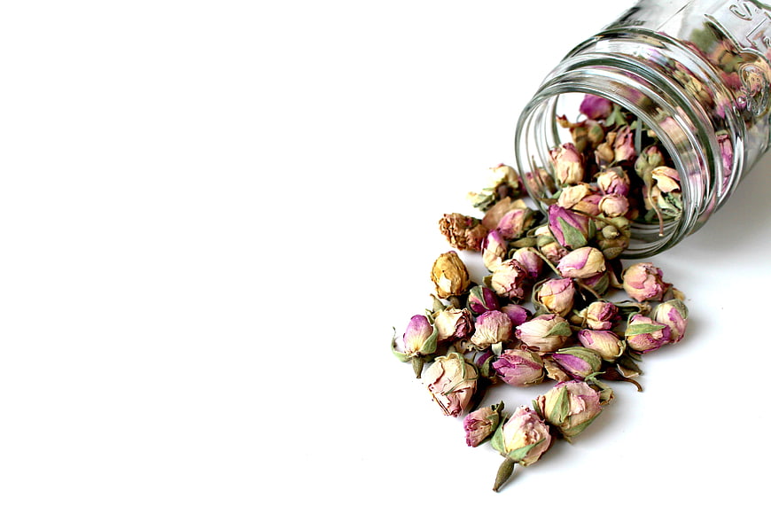 Dried rosebuds spilling from glass jar on white background