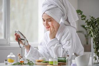 Woman in white robe applying skincare cream while looking in mirror