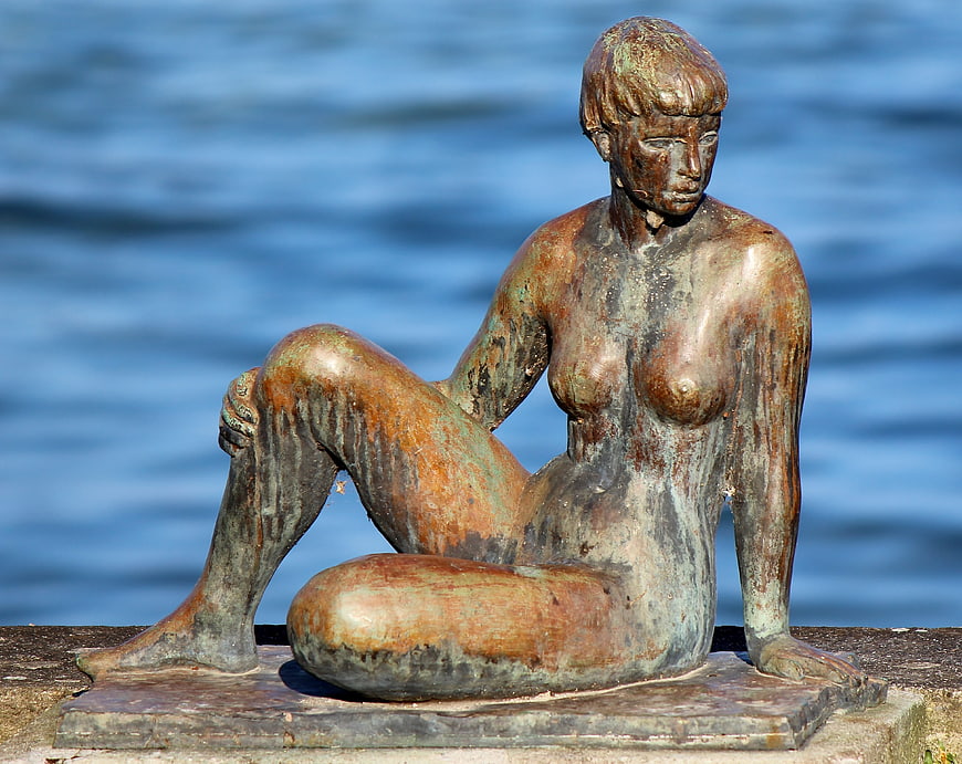 Weathered Bronze Female Sculpture Seated By Lake