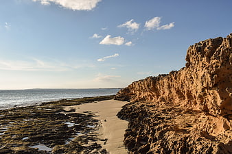 Sandy path along rugged coastal cliffs and calm sea