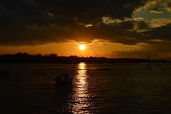 Dramatic sunset over water with silhouetted boats and clouds
