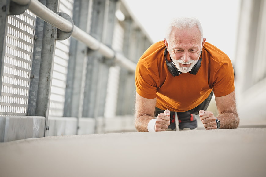 Senior man doing plank exercise outdoors with headphones