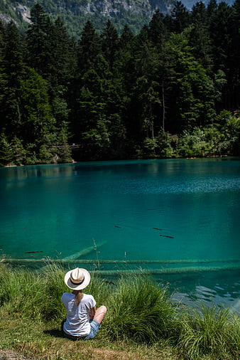 Woman in Hat Sitting by Turquoise Alpine Lake