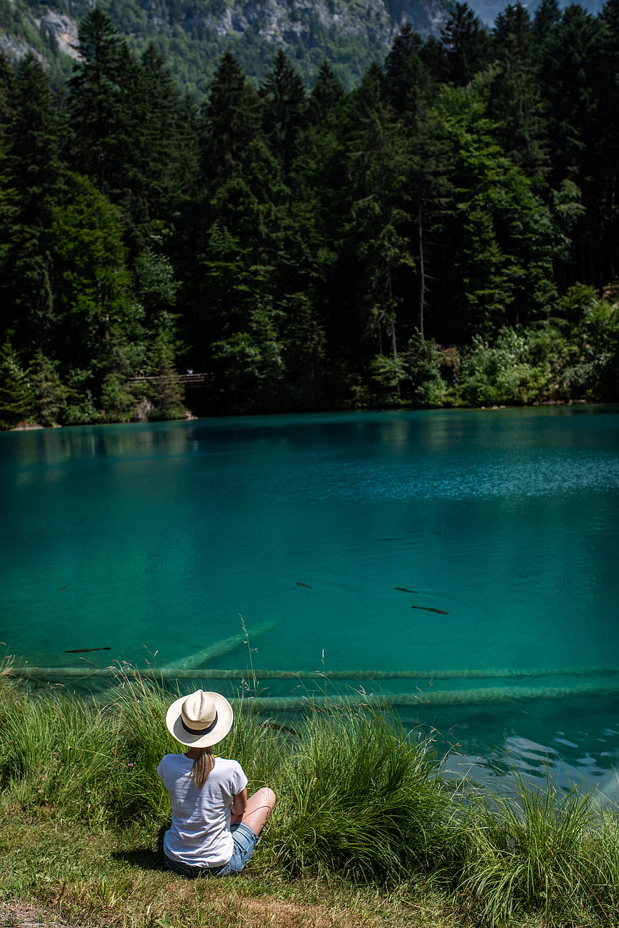 Woman in Hat Sitting by Turquoise Alpine Lake