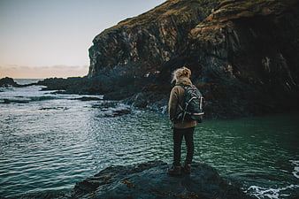 Hiker with Backpack Standing on Rocky Coastline at Sunset