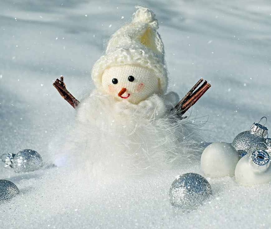 Cute handmade snowman doll with silver ornaments in snow