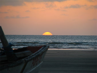 Sunset over ocean with fishing boat on beach