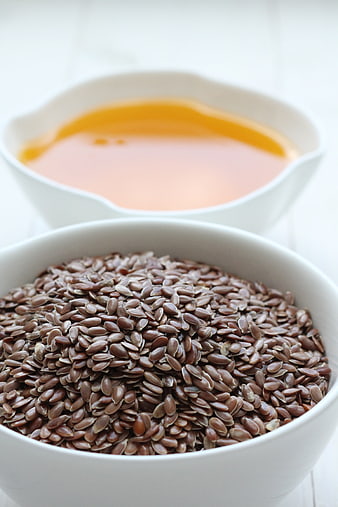 Bowl of brown flaxseeds and flaxseed oil on white background