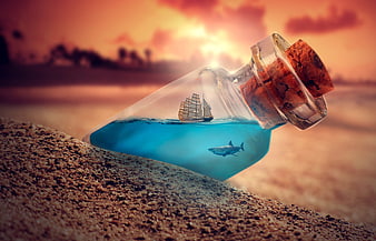 Glass bottle with miniature ship and shark on sandy beach at sunset